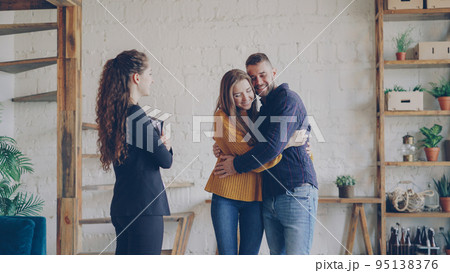 Real estate buyers are getting keys from housing agent after successful deal hugging with happiness and shaking hands to female broker. Real estate buyers are getting keys from housing agent after successful deal hugging with happiness and shaking hands to female broker. 95138376