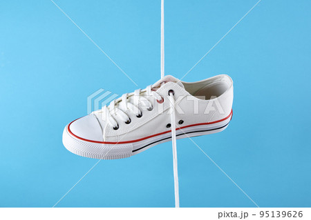 White female sport sneakers with shoe lace against blue background, Casual trendy shoes closeup, Creative minimal design with copy space White female sport sneakers with shoe lace against blue background, Casual trendy shoes closeup, Creative minimal design with copy space 95139626