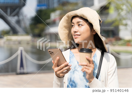 スマホと紙コップを持って街ブラを楽しむ若い女性 久屋大通公園にて 95140146
