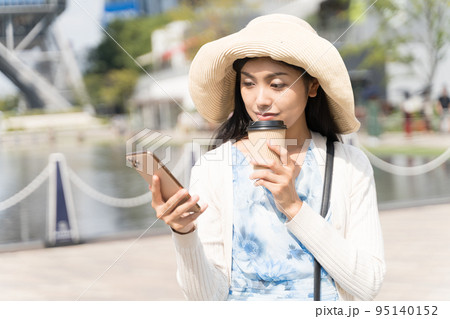 スマホと紙コップを持って街ブラを楽しむ若い女性 久屋大通公園にて 95140152