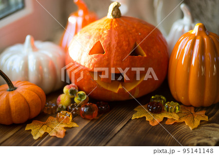 Orange and white pumpkins and jack lantern with his eyes and mouth cut out on a wooden table with yellow autumn maple leaves, berries. Autumn mood, halloween, home decor Orange and white pumpkins and jack lantern with his eyes and mouth cut out on a wooden table with yellow autumn maple leaves, berries. Autumn mood, halloween, home decor 95141148