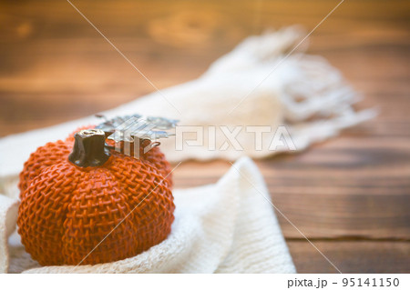 Orange pumpkin wrapped in a warm white plaid with lights of garlands on a wooden table with copyspace. Autumn mood, halloween, harvest, thanksgiving, home decor and cozy. Selective focus Orange pumpkin wrapped in a warm white plaid with lights of garlands on a wooden table with copyspace. Autumn mood, halloween, harvest, thanksgiving, home decor and cozy. Selective focus 95141150
