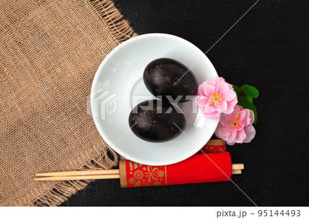 Black eggs, sakura flowers and chopsticks on a dark background 95144493