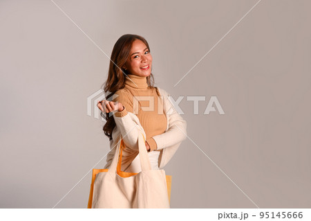 Elegant woman in warm sweater carrying tote bags standing over grey background Elegant woman in warm sweater carrying tote bags standing over grey background 95145666