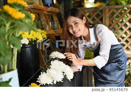 Successful small business entrepreneur in apron standing with flowers at rustic flower shop Successful small business entrepreneur in apron standing with flowers at rustic flower shop 95145670