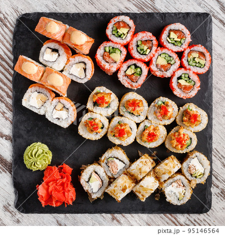 Large sushi set of various sushi rolls is served on black square metal slate. Large sushi set of various sushi rolls is served on black square metal slate. 95146564
