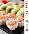 Sushi roll covered with chopped salmon and caviar is served on rectangular black slate. 95146569