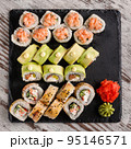 Large sushi set of various sushi rolls is served on black square metal slate. 95146571