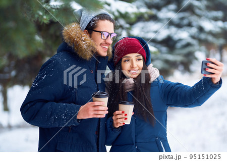 winter holidays, hot drinks and people concept. happy young couple with coffee in winter forest. winter holidays, hot drinks and people concept. happy young couple with coffee in winter forest. 95151025