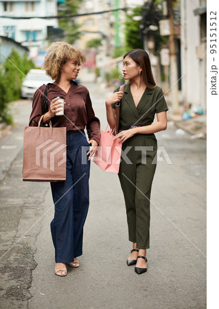 Young girls with shopping bags talking to each other while walking in the city after shopping Young girls with shopping bags talking to each other while walking in the city after shopping 95151512
