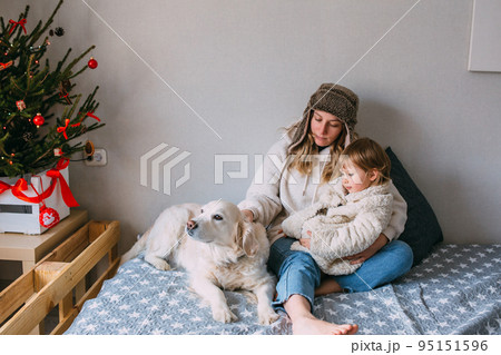 Mom and daughter comfortably cuddle at home with their pet Labrador Retriever Mom and daughter comfortably cuddle at home with their pet Labrador Retriever 95151596