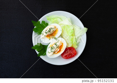 Hard boiled eggs with mayonnaise, lettuce and tomatoes on a plate on a dark background Hard boiled eggs with mayonnaise, lettuce and tomatoes on a plate on a dark background 95152131