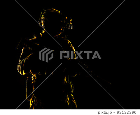 Army special forces elite soldier with hidden behind mask and glasses face, battle helmet, tactical radio headset, standing with assault rifle equipped silencer in darkness, contour shot 95152590