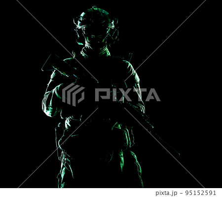 Army special forces elite soldier with hidden behind mask and glasses face, battle helmet, tactical radio headset, standing with assault rifle equipped silencer in darkness, contour shot 95152591