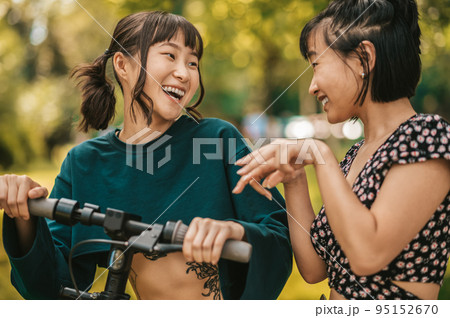 Two smiling girls with a scooter in the park 95152670