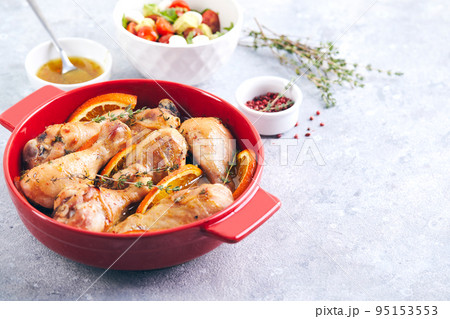 Chicken drumsticks with oranges and thyme baked in red round baking dish 95153553