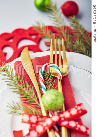 Christmas festive table setting with white plates and gold cutlery, red linen napkin, fir branches, red and green balls 95153560