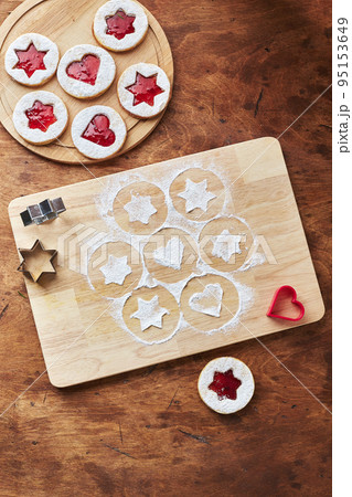 Wooden cutting board with powdered sugar and Linzer cookies, baking decoration process 95153649