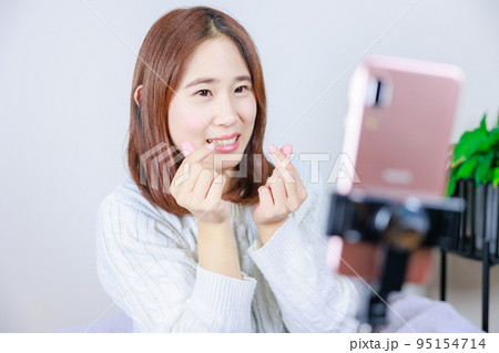 携帯電話の前で指ハートを作る女性 95154714