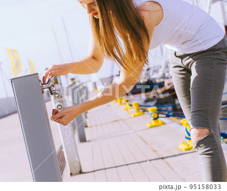 Woman drinking water from tap in marina. 95158033