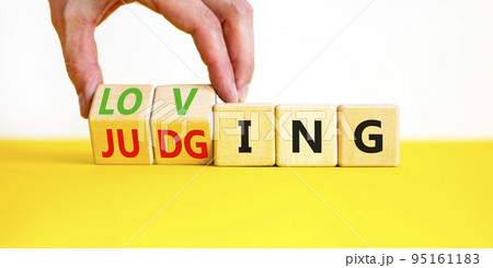 Loving or judging symbol. Concept words Loving or Judging on wooden cubes. Businessman hand. Beautiful yellow table white background. Business loving or judging concept. Copy space. Loving or judging symbol. Concept words Loving or Judging on wooden cubes. Businessman hand. Beautiful yellow table white background. Business loving or judging concept. Copy space. 95161183