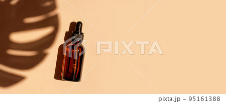 Amber glass dropper bottle on beige background with tropical leave shadow. Pipette with serum, oil, retinol, hyaluronic acid. Healthcare beauty product. Eco-friendly anti-age cosmetics. Amber glass dropper bottle on beige background with tropical leave shadow. Pipette with serum, oil, retinol, hyaluronic acid. Healthcare beauty product. Eco-friendly anti-age cosmetics. 95161388
