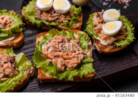 Delicious fresh sandwiches with toast, canned salmon, salad and quail eggs Delicious fresh sandwiches with toast, canned salmon, salad and quail eggs 95163480