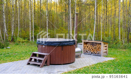 Modern hot tub with a wooden frame in the garden near the forest Modern hot tub with a wooden frame in the garden near the forest 95163641