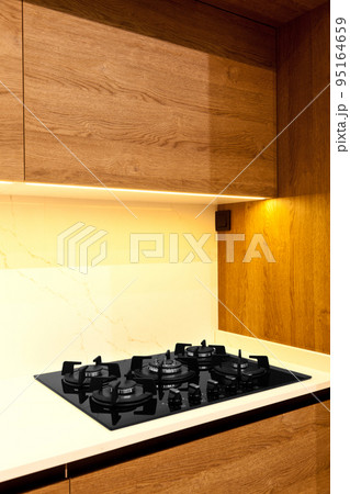 Modern brown wood oak kitchen cabinet equipment, white granite countertops and glass gas stove in a home Modern brown wood oak kitchen cabinet equipment, white granite countertops and glass gas stove in a home 95164659