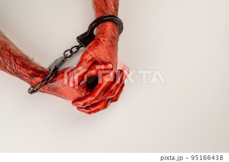 Bloodied male hands in handcuffs, folded on a white table. Bloodied male hands in handcuffs, folded on a white table. 95166438