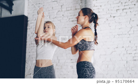 Professional yoga instructor is teaching new student to do arms twists while having individual practice in light wellness studio. Girls are laughing during exercises, relaxing atmosphere. Professional yoga instructor is teaching new student to do arms twists while having individual practice in light wellness studio. Girls are laughing during exercises, relaxing atmosphere. 95170664