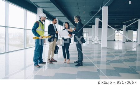 Multi-ethnic group of businesspeople male and female are talking and studying blueprint indoors in modern commercial building. Business and communication concept. Multi-ethnic group of businesspeople male and female are talking and studying blueprint indoors in modern commercial building. Business and communication concept. 95170667