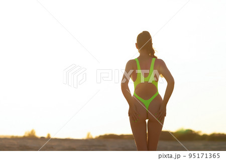 Unrecognizable sensual woman in swimsuit walking on sandy shore at sundown 95171365