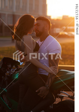 Couple hugging near motorbike at sunset 95172764