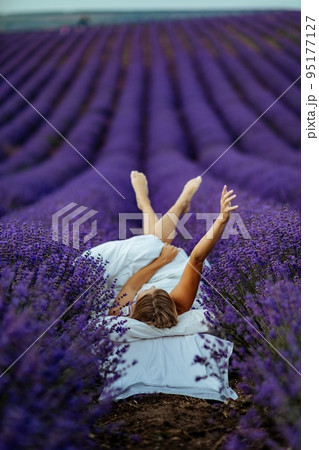 A middle-aged woman lies in a lavender field and enjoys aromatherapy. Aromatherapy concept, lavender oil, photo session in lavender 95177127