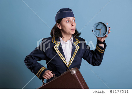 Stewardess running late at airport, holding retro alarm clock, carrying baggage. Airplane flight attendant, overslept, looking at time, air hostess hurry up at work with luggage 95177511