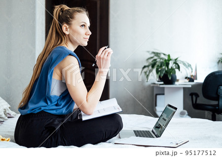 Job interview, Finding New Job. Young woman writing in Planner diary notes about job interview sitting near laptop on the bed at home Job interview, Finding New Job. Young woman writing in Planner diary notes about job interview sitting near laptop on the bed at home 95177512