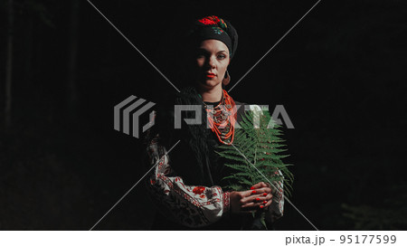 Authentic woman in traditional ukrainian handkerchief, necklace and costume with fern in forest at 95177599