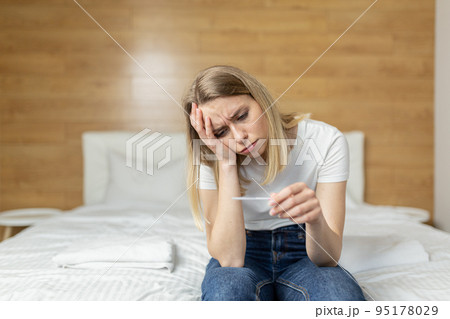 Young beautiful woman at home sitting on the couch, holding a quick pregnancy test in her hands, upset, shocked, learned about pregnancy, thinks confused Young beautiful woman at home sitting on the couch, holding a quick pregnancy test in her hands, upset, shocked, learned about pregnancy, thinks confused 95178029
