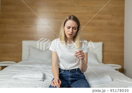 Young beautiful woman at home sitting on the couch, holding a quick pregnancy test in her hands, upset, shocked, learned about pregnancy, thinks confused 95178030