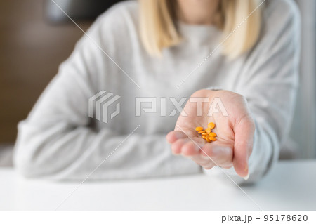 Close-up shot of a woman's hand holding a few yellow pills 95178620