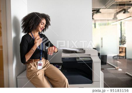 Curly-haired young woman near xerox in the office waiting for somebody 95183156