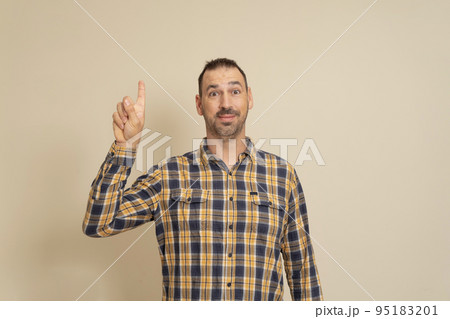 Smiling attractive man in plaid shirt posing isolated on beige wall background, studio portrait. People candid emotions lifestyle concept. Mock up copy space. Pointing the index finger up Smiling attractive man in plaid shirt posing isolated on beige wall background, studio portrait. People candid emotions lifestyle concept. Mock up copy space. Pointing the index finger up 95183201