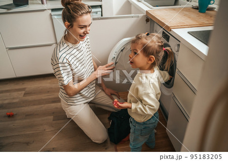 Female and her child putting dirty clothes into the washer 95183205
