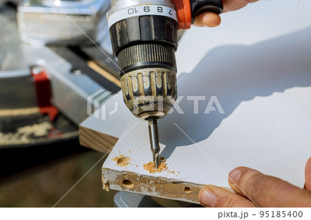 Carpenter drilling wood boards into using screwdriver for purpose of connecting them in construction process. Carpenter drilling wood boards into using screwdriver for purpose of connecting them in construction process. 95185400