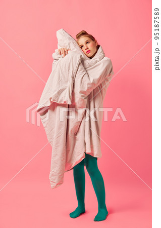 Beautiful young girl wrapped in soft blanket standing isolated over pink background. Comfrort, fashion, art, creativity Beautiful young girl wrapped in soft blanket standing isolated over pink background. Comfrort, fashion, art, creativity 95187589