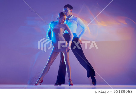 Art in motion. Flexible adorable ballroom dancers in stage attires dancing isolated on purple background in neon mixed light. Music, dance, emotions 95189068