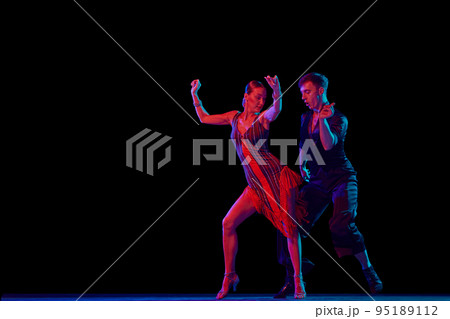 Stylish ballroom dancers couple in gorgeous outfits dancing in sensual pose on dark background in neon light. Concept of art, music, dance, emotions. Stylish ballroom dancers couple in gorgeous outfits dancing in sensual pose on dark background in neon light. Concept of art, music, dance, emotions. 95189112