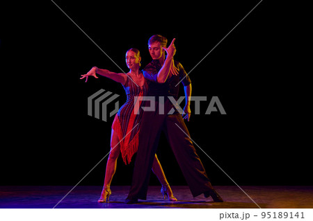 Stylish ballroom dancers couple in gorgeous outfits dancing in sensual pose on dark background in neon light. Concept of art, music, dance, emotions. Stylish ballroom dancers couple in gorgeous outfits dancing in sensual pose on dark background in neon light. Concept of art, music, dance, emotions. 95189141