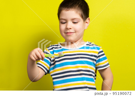 A handsome boy of 4 years old holds a toothbrush on a yellow background and laughs, copy space for text 95190072
